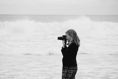 Side view of woman photographing at beach