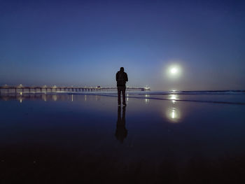 Rear view of silhouette man standing in water at sunset