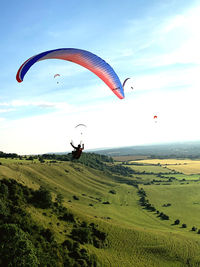 Scenic view of field against sky with a red paraglider coming in to land. 