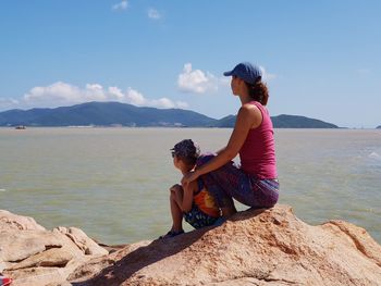 Side view of woman sitting on mountain against sky