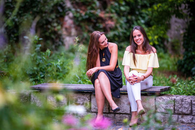 Full length of smiling young woman sitting against plants