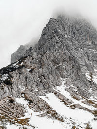 Tiny human walking on snow covered path under magnificent misty mountain