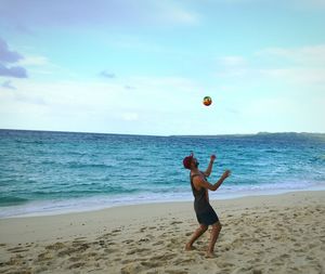 Side view of man playing with ball at beach against blue sky