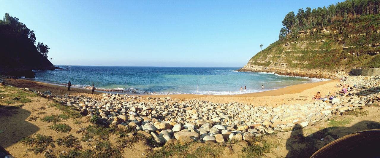 sea, beach, horizon over water, water, clear sky, shore, tranquil scene, sand, scenics, tranquility, copy space, beauty in nature, coastline, nature, blue, incidental people, sunlight, rock - object, idyllic, vacations