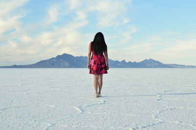 Rear view of woman standing on salt flat against sky