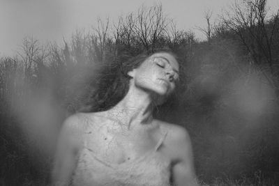 Double exposure of woman with eyes closed and bare trees