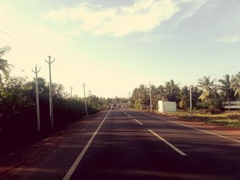 Empty road along trees and against sky