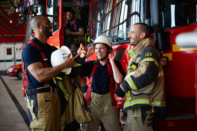 Happy firefighters discussing while standing by fire truck in fire station