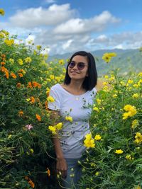 Young woman wearing sunglasses standing amidst yellow flowers against sky