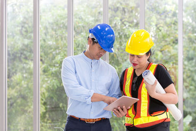 Coworkers discussing over tablet computer while standing against window in office