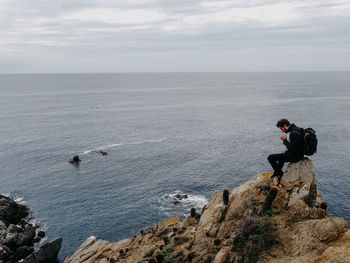 People on rocks by sea against sky