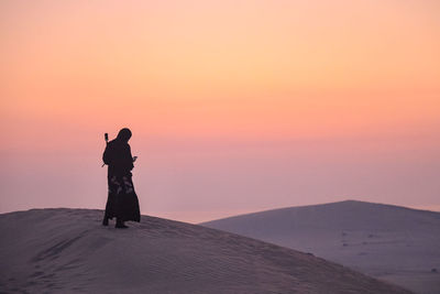 Silhouette woman standing on shore against sky during sunset