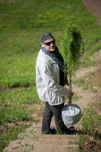 Portrait of man holding plants while standing on field