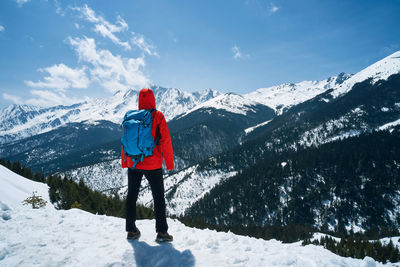 Rear view of man standing on snowcapped mountain against sky