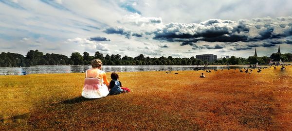 Rear view of couple sitting on shore against sky