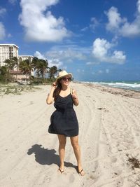 Smiling young woman standing on sandy beach against sky