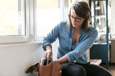 Businesswoman removing laptop from bag while sitting on bench in home office