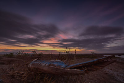 Abandoned boat on beach against sky during sunset