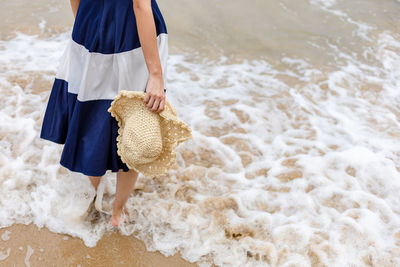Low section of woman standing at sea shore with hat
