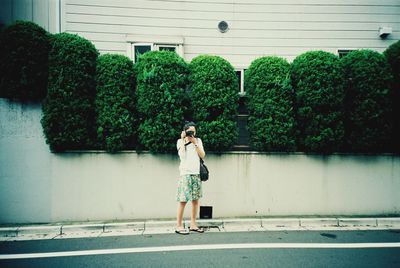 Woman photographing on sidewalk against building