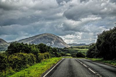 Road by trees against dramatic sky