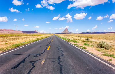 Empty road amidst field against sky