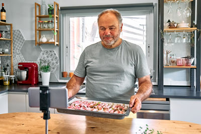 Man blogger preparing young green asparagus sprouts wrapped in bacon on wooden table in the kitchen.