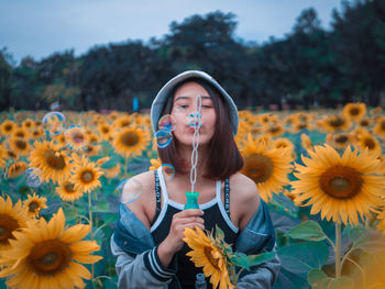 Young woman blowing bubbles amidst flowering sunflowers