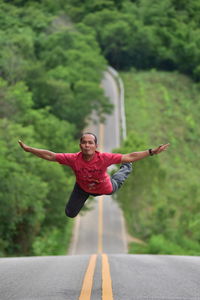 Portrait of smiling young woman with arms outstretched on road