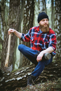 Portrait of man sitting on tree trunk in forest