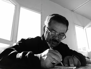 Man writing letter at table while sitting against window