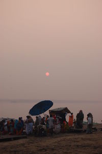 People at beach against sky during sunset