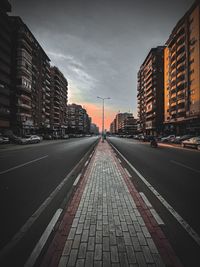 Road by buildings against sky during sunset