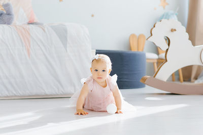 Cute baby in a pink dress keeps crawling on all fours in the children's room on the floor