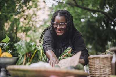 Smiling female vendor with braided hair arranging vegetables at market