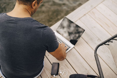 High angle view of man using laptop while sitting on jetty