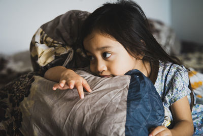 Cute girl looking away while relaxing on bed at home