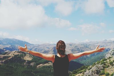 Portrait of young woman with arms outstretched against mountain range