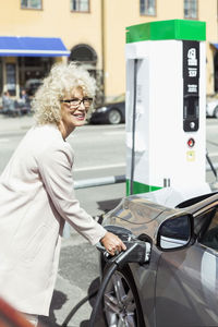 Smiling senior woman filling car with petrol at gas station