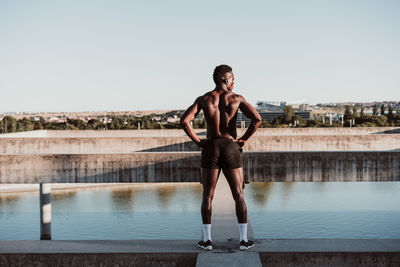 Male athlete with hand on hip standing against sky during sunny day