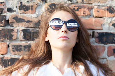 Woman wearing sunglasses with freedom text against brick wall