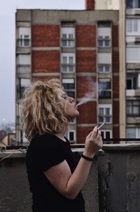 Side view of young woman smoking cigarette in building terrace 
