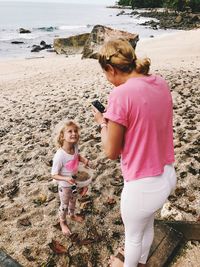 Full length of mother photographing daughter with mobile phone at beach