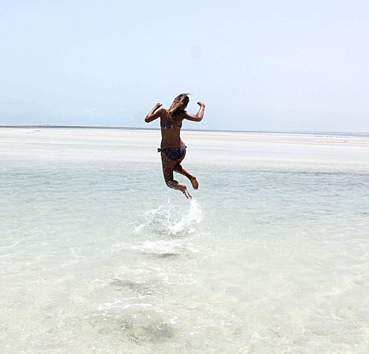 full length, water, lifestyles, leisure activity, jumping, sea, mid-air, enjoyment, fun, vacations, beach, arms outstretched, vitality, young adult, motion, clear sky, freedom, carefree