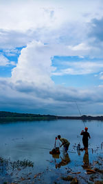 People fishing in lake against sky