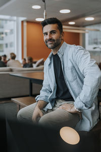 Portrait of confident mature businessman sitting on desk in office