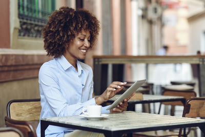 Smiling woman with afro hairstyle sitting in outdoor cafe using tablet