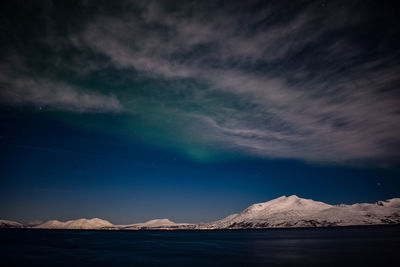 Scenic view of sea by snowcapped mountains against sky at night