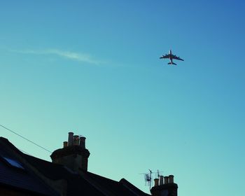 Low angle view of building against airplane flying in blue sky