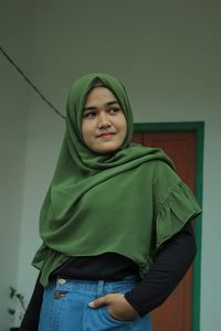 Portrait of smiling young woman standing against wall